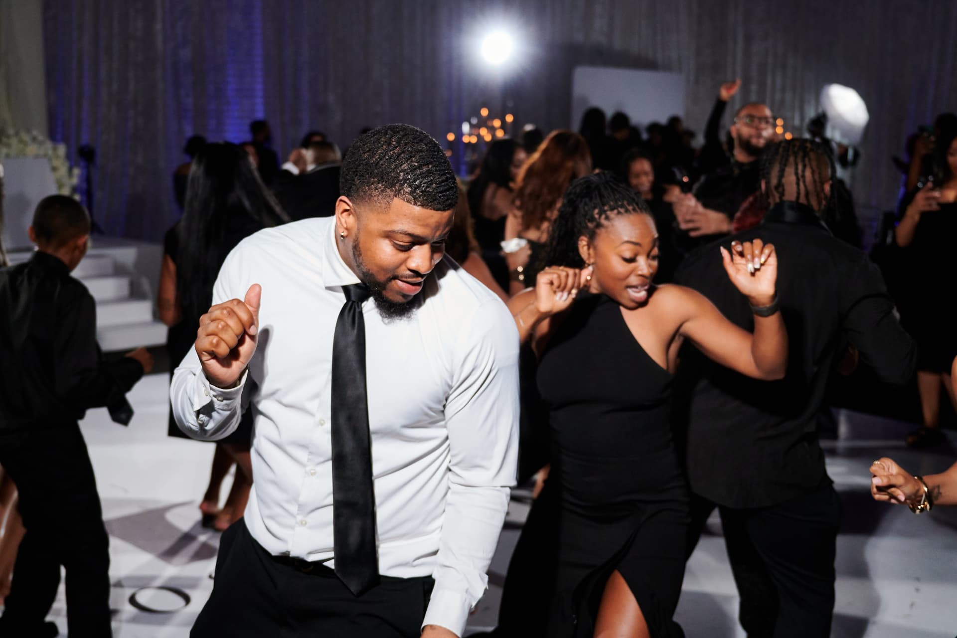 Guests dancing at a packed formal reception with elegant floral decor and string lights